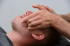 Ein Patient liegt auf dem Rücken, während ihm die Kiefermuskulatur massiert wird