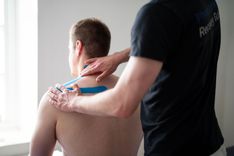 Ein Patient bekommt ein Tape auf den Rücken geklebt.